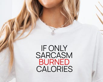 Puede incluir: Camiseta blanca con el texto "IF ONLY SARCASM BURNED CALORIES" en negro y rojo. La camiseta es de cuello redondo y la lleva puesta una persona. La persona lleva un collar plateado.