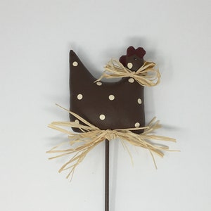 May include: A brown chicken figurine with white polka dots and a straw nest. The chicken has a red comb and is attached to a brown stick.