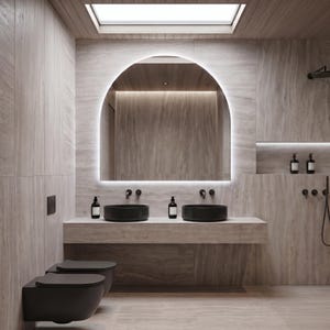 May include: A modern bathroom with a neutral color palette. The focal point is a large, arched mirror with integrated lighting. Two black vessel sinks sit atop a stone countertop. The room includes a toilet, shower, and wooden ceiling.