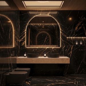 May include: A modern bathroom with black marble walls and flooring, featuring a large arched mirror with a warm light. Two black vessel sinks sit on a light-colored countertop. The room includes two black toilets and a wooden ceiling.