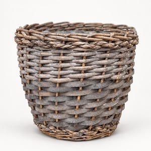 May include: A round, tapered basket woven from weathered grey-brown willow branches. The structure features a thick, braided rim and a dense, interlaced pattern of flat and rounded wooden strips, creating a sturdy, open-top container.