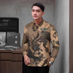 Op de afbeelding: Een overhemd met lange mouwen met een bruin en beige batikpatroon met bloemen- en vogelmotieven. Het overhemd heeft een klassieke kraag en wordt gedragen met een zwarte broek. Het ontwerp van het overhemd bevat teal en donkerblauwe accenten.