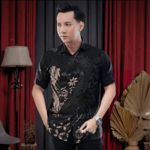 Könnte beinhalten: Schwarzes kurzärmeliges Hemd mit Batikmuster. Das Hemd hat ein detailliertes Design mit floralen und geometrischen Elementen in Schwarz- und Beigetönen. Das Hemd hat eine Knopfleiste und einen klassischen Kragen.