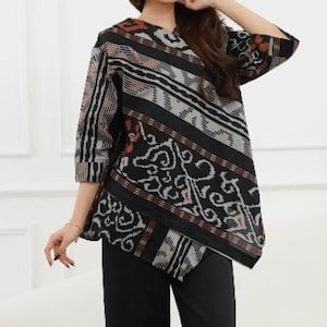 Op de afbeelding: Een zwart, grijs en bruin patroon top met driekwart mouwen. De top heeft een unieke asymmetrische zoom en een mix van geometrische en bloemmotieven. De stof lijkt een geweven materiaal te zijn.