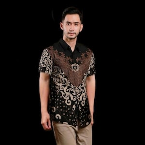 Op de afbeelding: Een zwart overhemd met korte mouwen en een bruin en beige bloemenpatroon. Het overhemd heeft een knoopsluiting en een klassieke kraag. Het ontwerp is ingewikkeld en gedetailleerd, met een symmetrische opstelling van bloemmotieven.