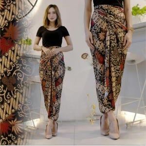 Op de afbeelding: Een zwarte top gecombineerd met een rok in batikstijl met een bruin, rood en crèmekleurig bloemmotief. De rok is gewikkeld en vastgeknoopt in de taille. Het model draagt nude-kleurige hakken.