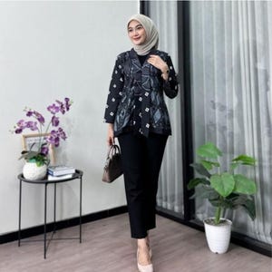 Puede incluir: Una mujer con una chaqueta estampada en blanco y negro sobre una blusa negra y pantalones negros. También lleva un pañuelo claro y un bolso marrón. El conjunto se completa con tacones de color claro.