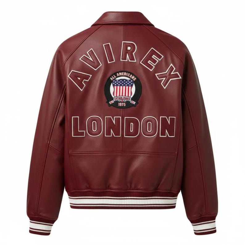 May include: A burgundy leather varsity jacket featuring a white collar and striped ribbed cuffs and hem. The back displays the text AVIREX in an arc, the word LONDON below, and a circular patch with an American flag and the text ALL AMERICANS ESTABLISHED 1975.