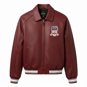 May include: A deep burgundy leather jacket featuring a classic collar, a full-length front zipper, and two side pockets. The chest displays an embroidered patch with the text AVIREX and a flag design. The cuffs and hem have white and burgundy stripes.