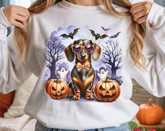 May include: White sweatshirt featuring a Halloween-themed dachshund wearing sunglasses and a bow tie, with jack-o'-lanterns, ghosts, and bats. The design has a spooky forest background with purple and black accents.