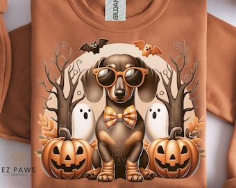 May include: A brown sweatshirt with a Halloween-themed graphic. The graphic features a dachshund wearing orange sunglasses and a plaid bow tie, flanked by pumpkins, ghosts, bats, and bare trees. The text "300 DPI HD IMAGE DIGITAL DOWNLOAD" is at the bottom.
