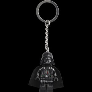 May include: A black Darth Vader Lego keychain with a silver metal ring and chain. The keychain features the iconic character's helmet and cape, with detailed printing on the torso. The background is solid black.