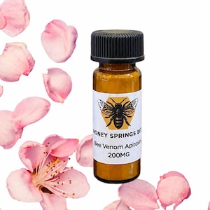 May include: A small amber glass bottle with a black cap, labeled Honey Springs Bee Bee Venom Apitoxin 200MG, surrounded by scattered pink flower petals. Text on the image reads Bee Powder Used in skincare to reduce wrinkles effectively.
