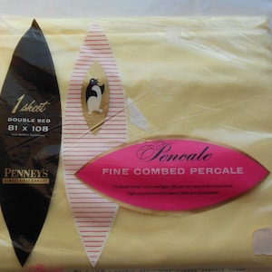 May include: A packaged double bed sheet in a pale yellow color. The packaging includes a black label with white text indicating the sheet size, and a pink label with the word "Pencale". A penguin graphic is also visible.