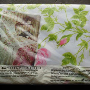 May include: A Martex no-iron percale sheet packaged in clear plastic. The fabric is white with a green leaf and pink rose floral pattern. A rectangular insert shows a bed with the sheet. Text includes product details and washing instructions.