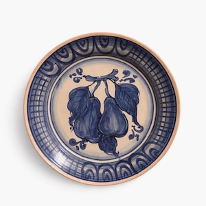 May include: A round ceramic plate with a hand-painted design. The plate features a beige center with a blue illustration of pears and leaves. The rim has a blue and white pattern, and the outer edge is a natural beige color.