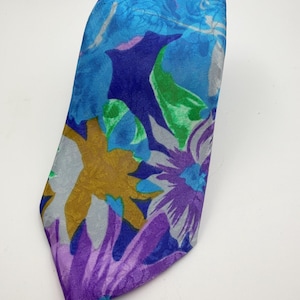 Könnte beinhalten: Eine gemusterte Krawatte mit floralem Design. Die Krawatte zeigt eine Mischung aus blauen, lila, grünen und goldenen Farbtönen. Das Design umfasst große, stilisierte Blumen und Blätter, was ein auffälliges Accessoire ergibt.