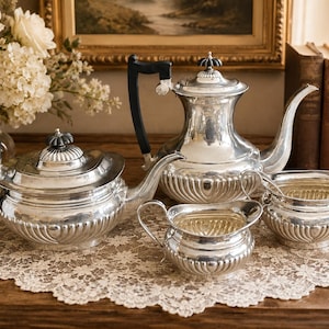 May include: A silver tea set comprising a teapot, a coffee pot, a creamer, and a sugar bowl. Each item features a polished metallic finish, a fluted base design, and black handles. The pots have matching lids with small, dark, decorative finials.