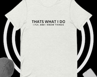 May include: Light heather gray t-shirt with the text "THATS WHAT I DO I FLY, AND I KNOW THINGS" in black. The shirt is a short-sleeved crew neck style.