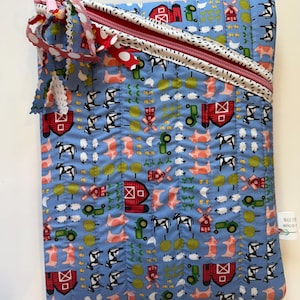 May include: A quilted fabric case with a farm animal pattern. The case features a light blue background with repeating images of cows, pigs, sheep, barns, and tractors. It has a red zipper and a decorative ribbon. The tag says "MADE FOR erica".