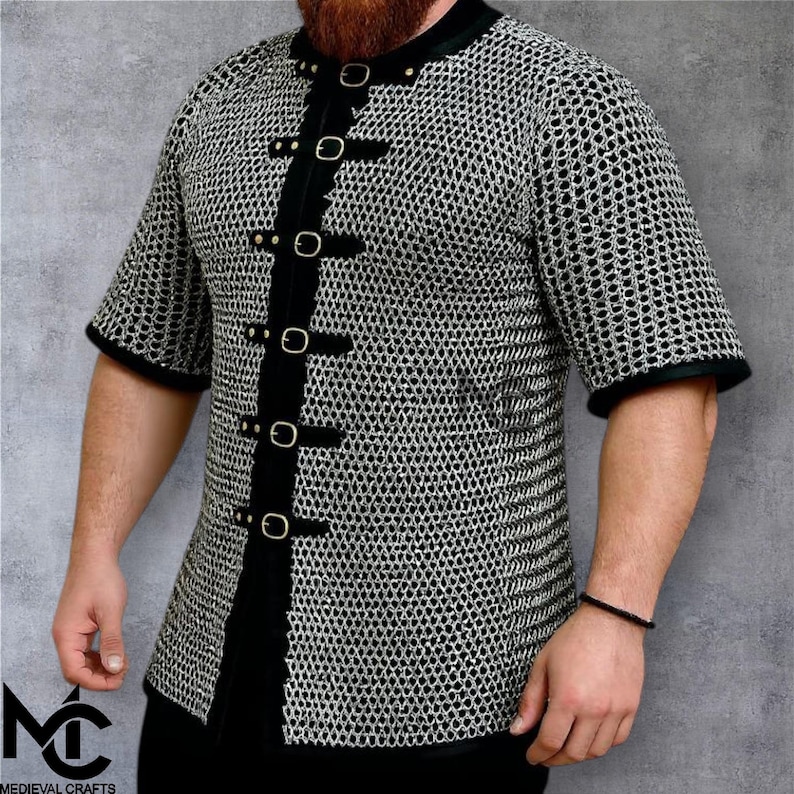 May include: A short-sleeved chainmail shirt with black trim and fasteners. The shirt has a black collar and is fastened with black straps and silver buckles. The image includes the logo "MEDIEVAL CRAFTS" in the bottom left corner.