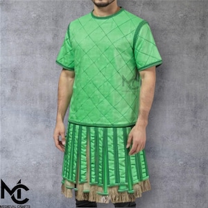 Könnte beinhalten: Ein grünes, gestepptes Kurzarm-Shirt und ein passender Rock. Das Shirt und der Rock sind hellgrün mit dunkelgrünen Zierleisten. Der Rock hat vertikale Streifen und einen Fransenbesatz. Das Medieval Crafts-Logo ist unten links sichtbar.