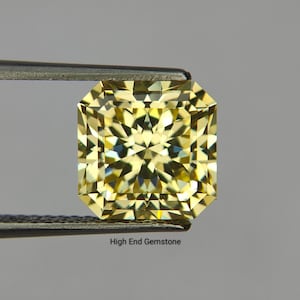 Può includere: Una gemma gialla e radiosa con taglio rettangolare, tenuta da una pinzetta. Le sfaccettature della gemma riflettono la luce, creando un'esposizione brillante. Il testo "High End Gemstone" è visibile in basso.