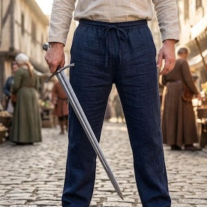 May include: A pair of dark blue linen trousers featuring an elastic waistband with a drawstring closure, worn with a light-colored long-sleeved shirt. A metal sword with a cross-guard is held in one hand, pointing downward toward the ground.