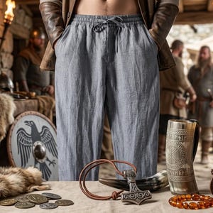 May include: Light blue drawstring trousers with a relaxed fit and an elastic waistband. The pants feature two side pockets and are made of a textured fabric. The trousers are worn with a brown leather jacket, showcasing a casual and comfortable style.
