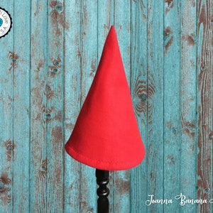 May include: A red felt gnome hat on a wooden stand. The hat is pointy and has a simple design. The stand is black and has a round base.