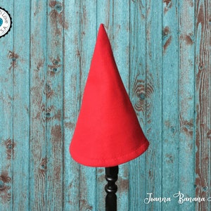 May include: A red felt gnome hat on a wooden stand. The hat is pointy and has a wide brim. The stand is black and has a decorative scroll design.