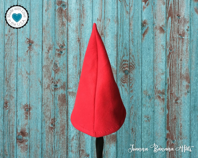 May include: A red felt gnome hat with a pointed top. The hat is sitting on a wooden surface.