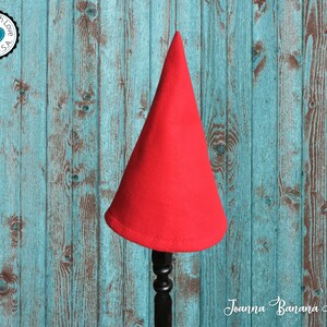 May include: A red felt cone-shaped hat on a wooden stand against a blue and brown woodgrain background. The hat is made in the USA with love.
