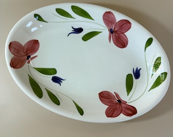 May include: Oval white ceramic platter with hand-painted floral design. Features maroon flowers, green leaves, and blue bell-shaped accents. A decorative serving dish for displaying food or as a decorative piece.