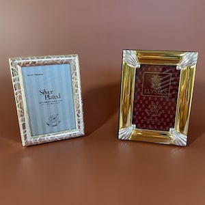 Może przedstawiać: Dwie dekoracyjne ramki na zdjęcia. Jedna jest posrebrzana z teksturowaną obwódką i napisem "Silver Plated". Druga ramka ma złoty obramowanie ze srebrnymi akcentami i bordowe wnętrze z napisem "ELYSEES".