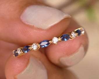May include: A gold ring featuring alternating blue and white gemstones. The ring's design includes oval-cut blue sapphires and round, clear diamonds. The gemstones are set in a delicate, thin band, creating a sparkling and elegant piece of jewelry.