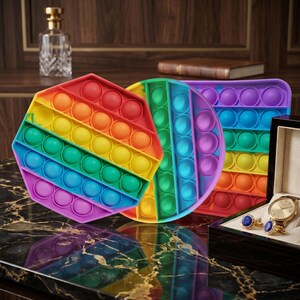 May include: Three colorful pop-it fidget toys in rainbow hues. The shapes include a hexagon, a circle, and a rectangle. The toys are made of silicone and have multiple bubble-like depressions that can be pushed in and out.