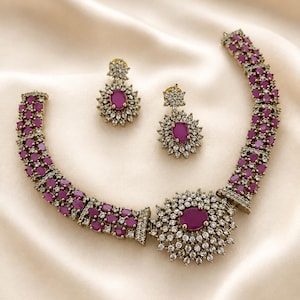 Peut inclure: Un ensemble de bijoux composé d'un collier et d'une paire de boucles d'oreilles assorties. Le collier présente une pierre centrale ovale magenta entourée de cristaux clairs, avec une bande de pierres magenta et de cristaux clairs. Les boucles d'oreilles.