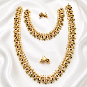 May include: A gold-toned jewelry set consisting of two necklaces and two matching earrings. Each piece features a repeating teardrop motif with a central deep red stone, surrounded by small white stones and accented with tiny green beads and pearls.