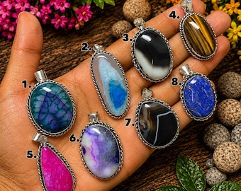 May include: Eight oval and teardrop-shaped gemstone pendants set in silver-toned metal frames, numbered one through eight. The stones feature various colors and patterns, including blue, pink, purple, black, white, and brown tiger's eye.