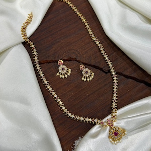 Peut inclure: Un collier doré et une paire de boucles d'oreilles assorties présentant un motif répétitif de pierres blanches transparentes et de petites pierres rouges. Le collier comprend un pendentif central avec une pierre rouge entourée de perles blanches.