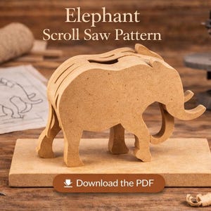 Op de afbeelding: Een houten olifant scroll saw patroon, geassembleerd en weergegeven op een houten basis. De olifant is lichtbruin met zichtbare snijlijnen. De afbeelding bevat de tekst "Elephant Scroll Saw Pattern" en een knop met de tekst "Download the PDF".