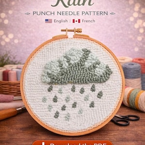 Op de afbeelding: Een punch needle patroon getiteld "Rain" met een wolk- en regendruppelontwerp. Het ontwerp is gestikt op witte stof en geplaatst in een houten borduurring. De tekst "Download the PDF" wordt op een knop onderaan weergegeven.