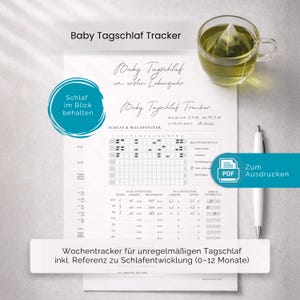 May include: A white printed baby sleep tracker chart with the text "Baby Tagschlaf Tracker" and "Schlaf im Blick behalten". A cup of tea and a pen are next to the chart. The chart includes a sleep and wake window.