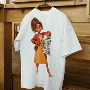 Peut inclure: Un t-shirt blanc &agrave; manches courtes avec une impression graphique repr&eacute;sentant une personne aux cheveux bruns boucl&eacute;s, portant un gilet rouille, une jupe jaune et des lunettes, tenant une haute pile de livres et un petit sac &agrave; bandouli&egrave;re marron.