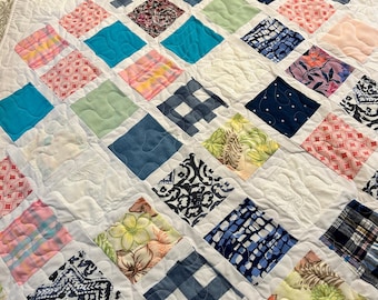 May include: A handmade quilt with a white background and a diamond pattern. Each diamond is a different color and pattern, including floral, plaid, and solid colors. The quilt is quilted with a wavy stitch.