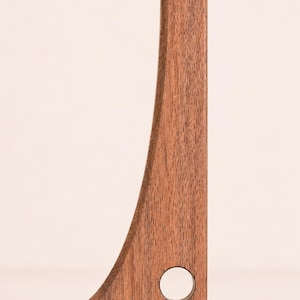 Könnte beinhalten: Ein vertikaler Regalträger aus Holz mit einer geraden Rückseite und einem geschwungenen Vorderprofil. Der Träger ist aus braunem Holz mit sichtbarer Maserung gefertigt und verfügt über eine kreisförmige Aussparung nahe der Basis.
