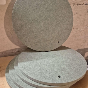 Könnte beinhalten: Ein Stapel von sechs grauen, kreisförmigen Holzplatten mit matter Oberfläche. Jede Platte hat ein kleines Loch am Rand. Die Platten liegen auf einer hellbraunen Holzoberfläche.