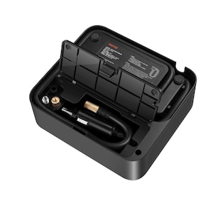 Puede incluir: Un compresor de aire portátil rectangular de color negro con una tapa superior abierta que revela un compartimento de almacenamiento. En su interior, se aprecian un cable de alimentación negro con un conector dorado y una boquilla metálica.