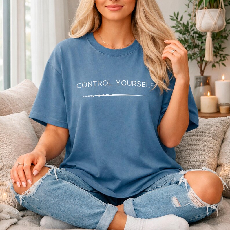 May include: A blue short-sleeved t-shirt featuring the white text "CONTROL YOURSELF" printed across the chest, accompanied by a horizontal white line graphic underneath the lettering. The shirt has a crew neckline and a relaxed fit.